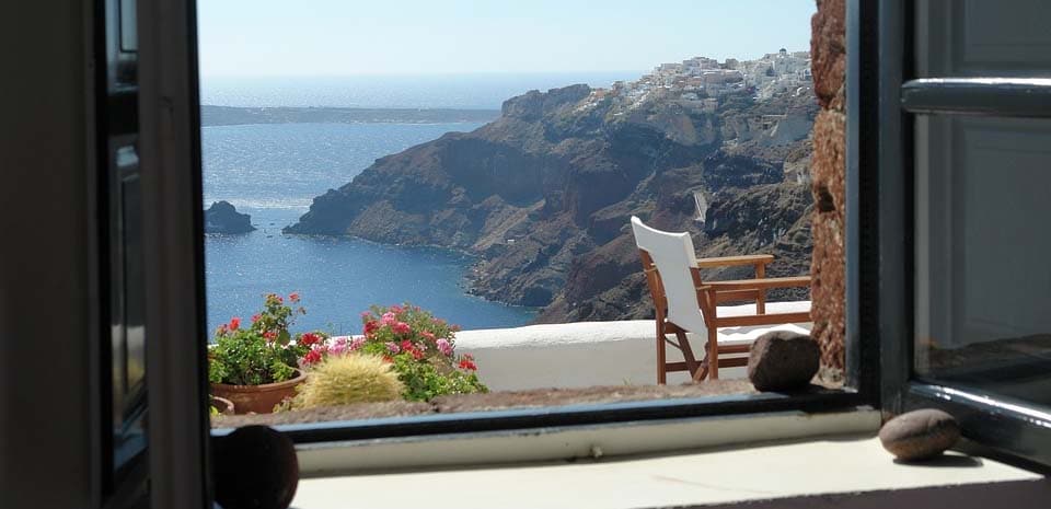 looking out a window onto a balcony overlooking mountains and ocean