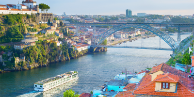 Panoramic view of the river valley in Porto, Portugal, as a river cruise ship prepares to pass under a bridge spanning the river valley