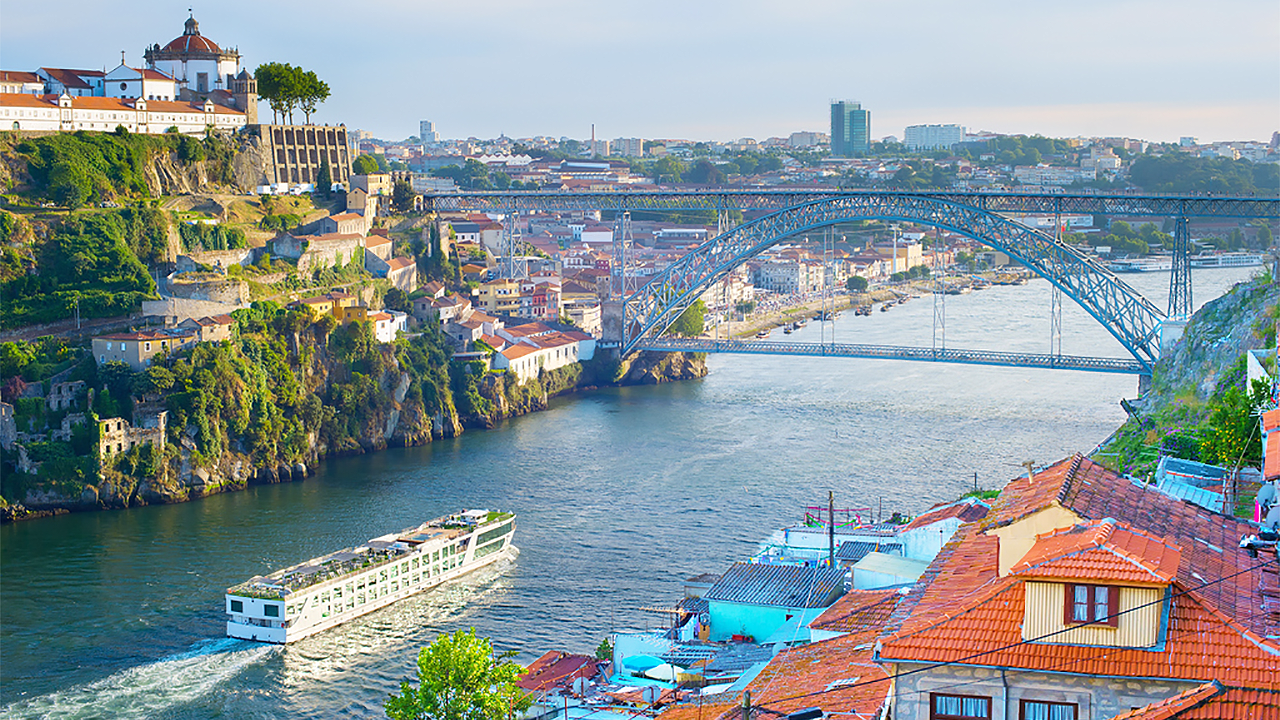 Panoramic view of the river valley in Porto, Portugal, as a river cruise ship prepares to pass under a bridge spanning the river valley