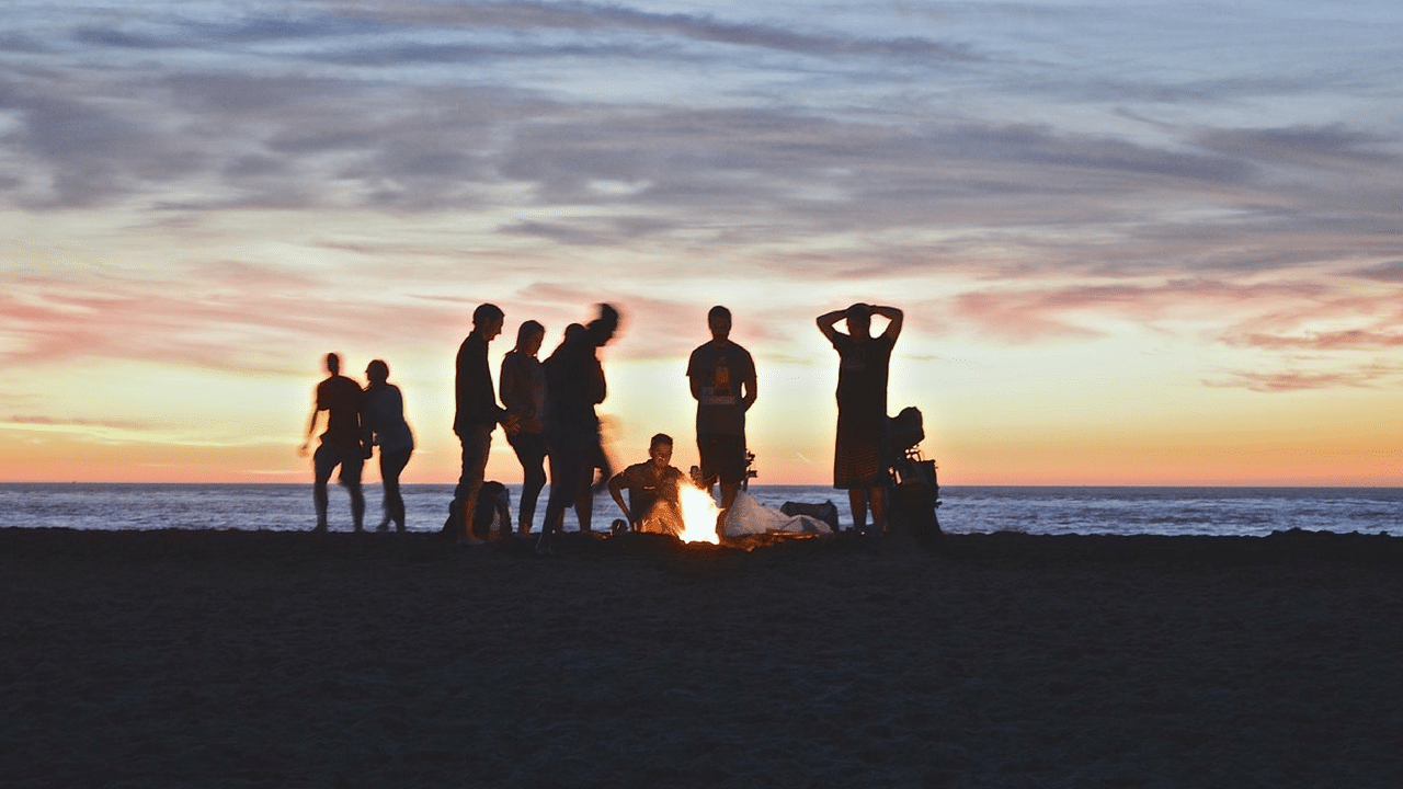 Friends enjoy a fire at the beach at sunst