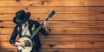 A man plays a banjo next to a wooden wall