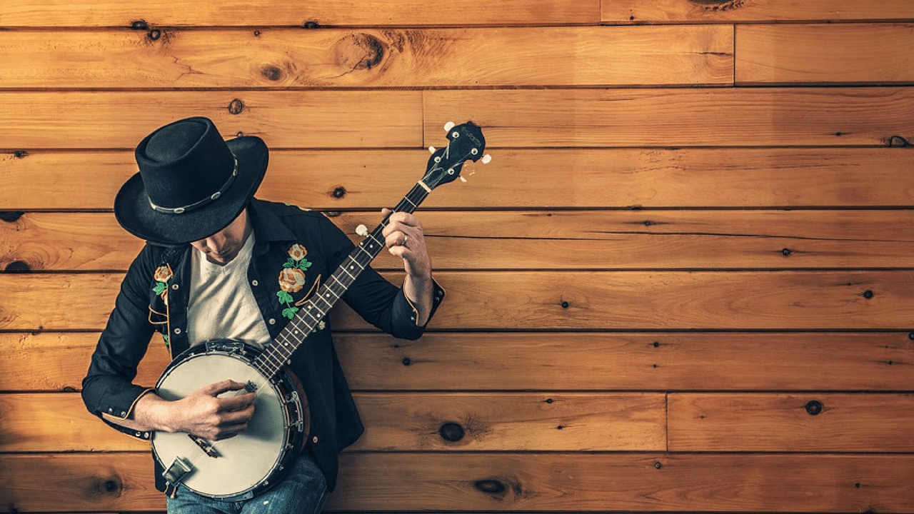 A man plays a banjo next to a wooden wall