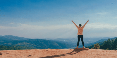 Person holding his arms in the air looking out over the mountains