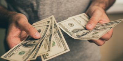 A man in a gray T-shirt holds dollars in his hands