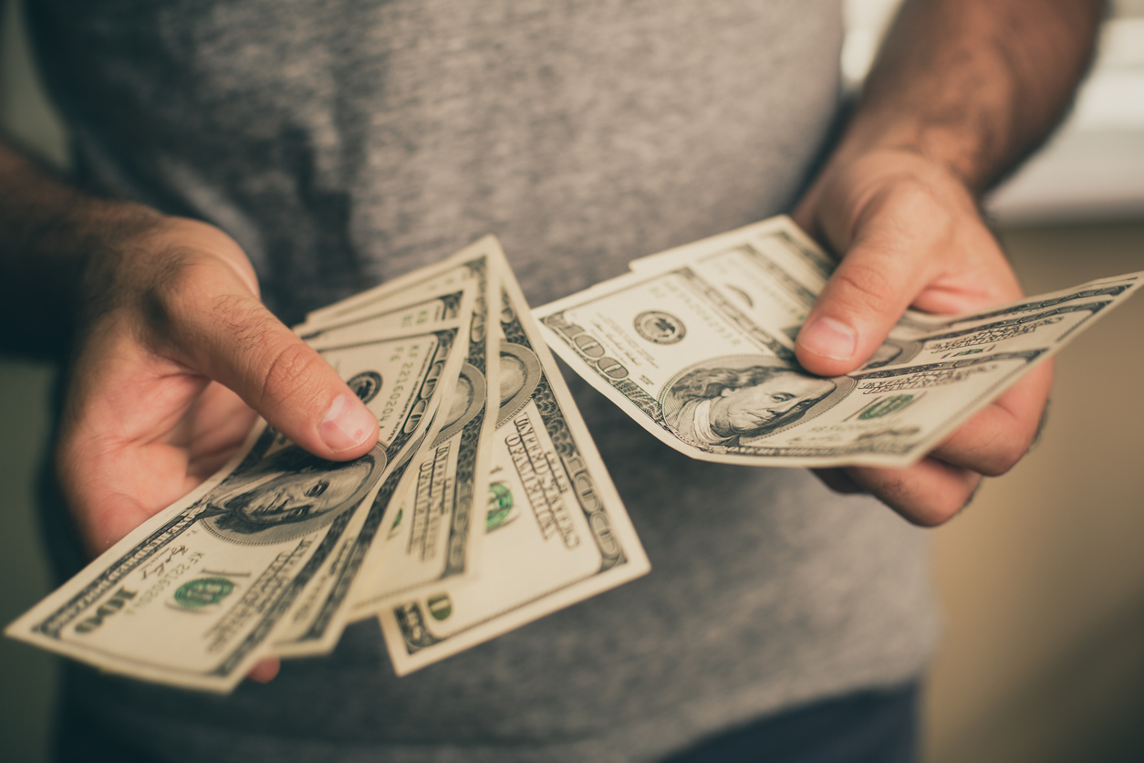 A man in a gray T-shirt holds dollars in his hands