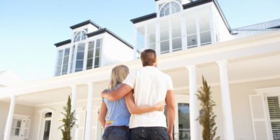 a couple looking up to their brand new home overseas, a white 2 story house with collums on the outside