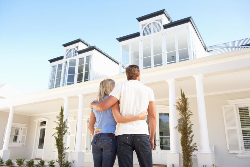 a couple looking up to their brand new home overseas, a white 2 story house with collums on the outside