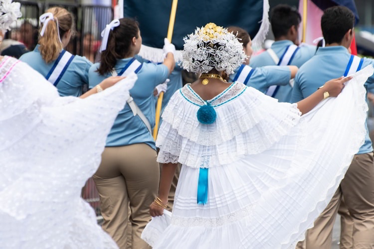 Woman wearing traditional white Panamanian dress and other people in the street during Panama National Day parade