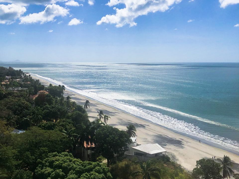 Bright blue sky on Coronado beach, Panama. There is salt and pepper sand, green trees, and a blue sea