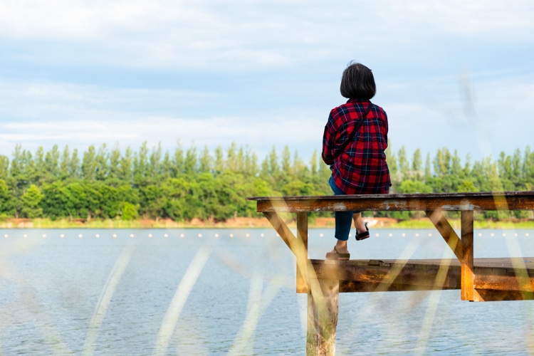 Senior retired woman sitting on the pier enjoying the view of lake