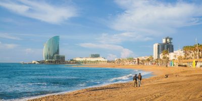 Pedestrians walk along Barceloneta Beach in Barcelona with colorful sky at sunrise