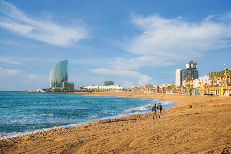 Pedestrians walk along Barceloneta Beach in Barcelona with colorful sky at sunrise